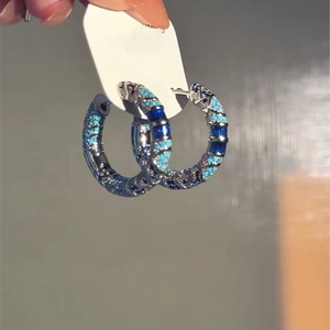 Macro detail of silver hoop earring with blue baguette and round zircon stones