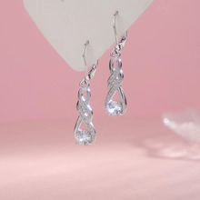 Detail of silver infinity earrings with sparkling zircon stones on a pink background
