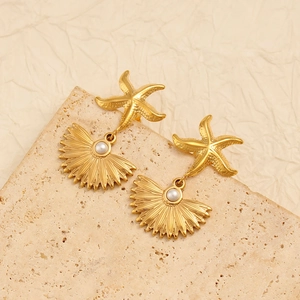 Golden starfish and shell drop earrings with white pearls on a textured background