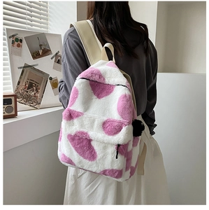Close-up of pink and white cow print plush backpack with soft faux fur and fluffy pom-pom