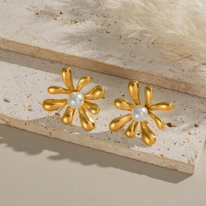 Close-up of elegant gold flower earrings with white pearls on rustic beige stone slabs