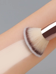 Macro shot of dual-ended makeup brush applying liquid foundation smoothly on skin