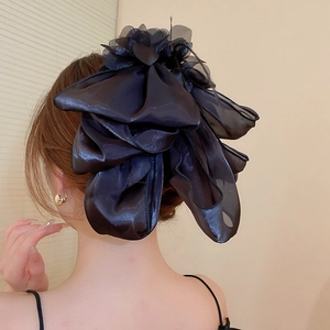 Gros plan d'une grande pince à cheveux nœud noir montrant la texture du tissu brillant