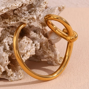 Artistic close-up of a 18K gold-plated knotted open bangle on natural stone and shell