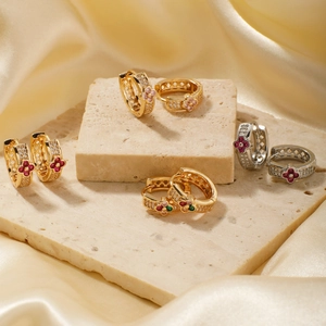 Macro shot of geometric hoop earrings with zircon four-leaf clover details on beige stone