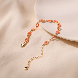 Detailed macro view of the gold-plated chain and orange enamel oval charms on the bracelet