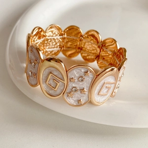 Gros plan d'un bracelet doré avec émail blanc, logo en lettre G et motifs de petites étoiles