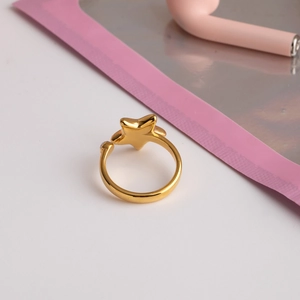 Détail d'une bague étoile dorée ajustable avec un petit diamant sur un fond rose doux