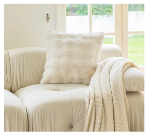 Detail of cream plush square pillow cover on leather sofa with knitted blanket