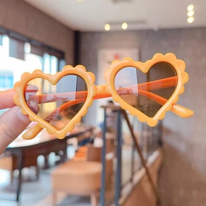 Close-up of orange heart-shaped kids sunglasses with wavy frames in a warm setting