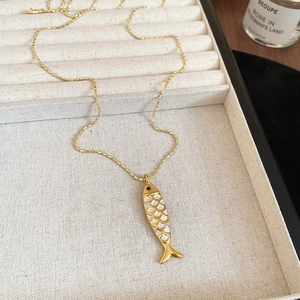 Detailed close-up of golden fish pendant with shell inlay and bamboo chain on display tray