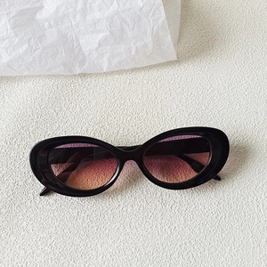 Detail of oval cat eye sunglasses with black frame and purple-orange gradient lenses
