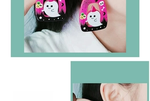 Close-up of pink Halloween acrylic earrings with ghost and pumpkin patterns on a model