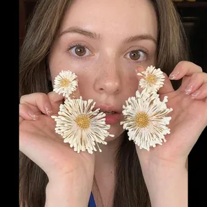 Close-up of oversized white daisy earrings featuring yellow centers on female model