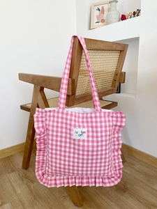 Pink checkered canvas tote bag with ruffle trim and a fun fun party label on a chair