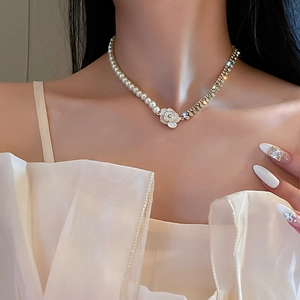 Détail du collier en perles et strass avec un pendentif en forme de rose blanche