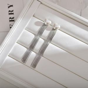 Macro view of long silver tassel earrings with heart-shaped pearls on white leather box