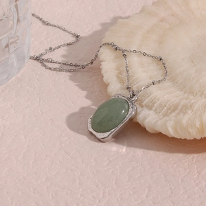 Macro shot of a green oval gemstone pendant with silver bead chain on white coral stone