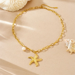 Gold plated stainless steel necklace with starfish pendant and pearl on sandy background
