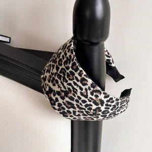 Detail shot of a wide leopard print headband hanging on a black bedpost with soft lighting