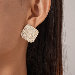 Close-up of square geometric stud earrings with pave crystals on a golden base