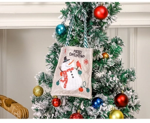 Detail of linen Christmas gift bag with snowman print hanging on a decorated tree