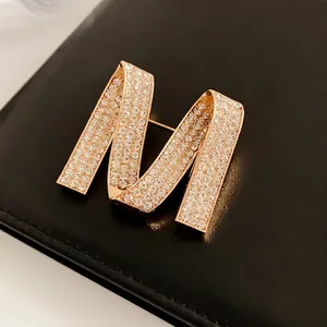 Luxury gold M-shaped brooch with sparkling rhinestones on black leather surface