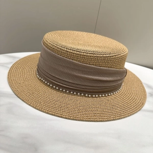 Detail of straw hat with pearl chain and dark khaki ribbon on marble surface