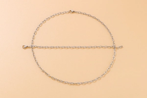 Macro shot of silver-toned paperclip chain necklace and bracelet on a peach background