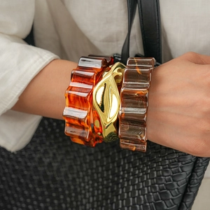 Close-up of amber resin wave bangles and a sculptural gold lava metal bracelet set