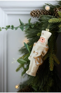 Nutcracker Christmas ornament in white and gold hanging on a pine tree branch