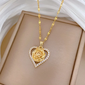 Macro shot of gold heart pendant with rose detail and zircons on white silk background