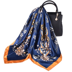 Close-up of floral satin scarf draped on a black leather handbag with a glossy finish