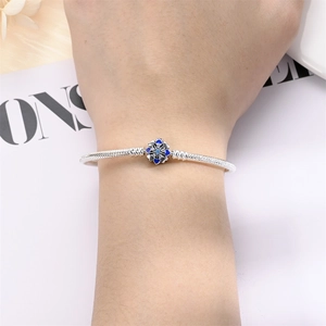 Detail of silver snake chain bracelet with blue flower charm on model's wrist