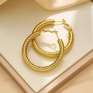 Detailed close-up of golden spiral hoop earrings on a luxury silk textured background