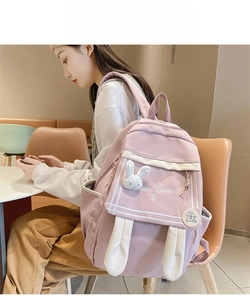 Close-up of pink backpack with cute plush rabbit ears and brand logo in a cozy setting