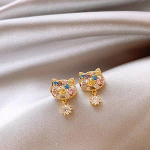 Macro shot of gold-plated cat-shaped stud earring with multicolor zircons on silk fabric