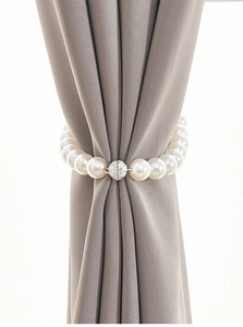 Detail of elegant magnetic pearl curtain tieback with sparkling rhinestone buckle on grey fabric