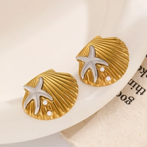 Detail of golden shell earrings with silver starfish and pearls on a ceramic plate