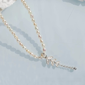 Macro shot of natural freshwater pearl necklace with silver leaf pendant on blue background