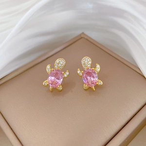 Detailed macro view of turtle earrings with pink crystals and gold finish on silk