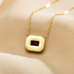 Detailed shot of a gold necklace with a red square zircon pendant on silk fabric