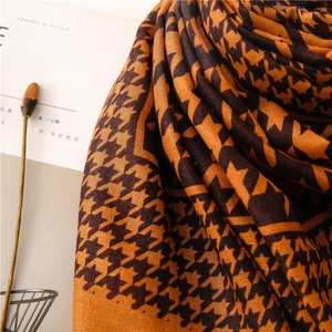 Detail of caramel houndstooth scarf texture with minimalist magazine and dried plant