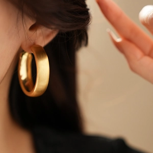 Dettaglio di orecchini a cerchio spessi placcati oro opaco per un look minimalista di lusso