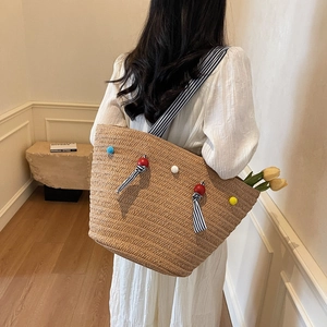 Large hand-woven straw tote bag with colorful pom-poms and striped shoulder straps