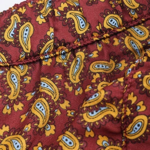 Macro shot of paisley print twill fabric detailing fine stitching on burgundy textile