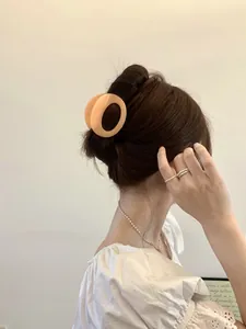 Detailed back view of a large matte apricot circular hair claw clip on a woman's bun hairstyle