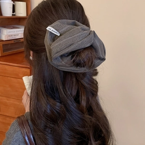 Macro shot of large grey striped fabric scrunchie with brand tag on hair ponytail