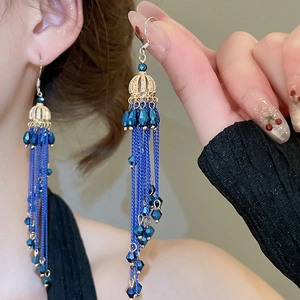 Detail of luxury long tassel drop earrings with blue crystals and gold-plated flower charms