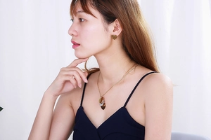 Gros plan d'un ensemble collier et boucles d'oreilles cœur doré porté par un modèle